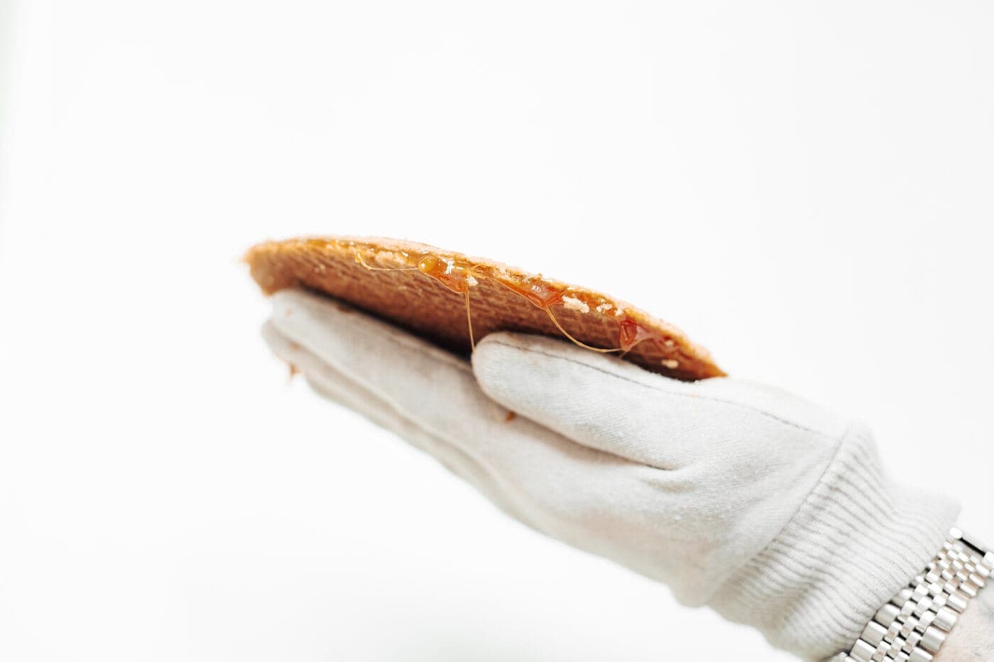 A stroopwafel held on its side, warm caramel syrup stretching between the two waffle layers