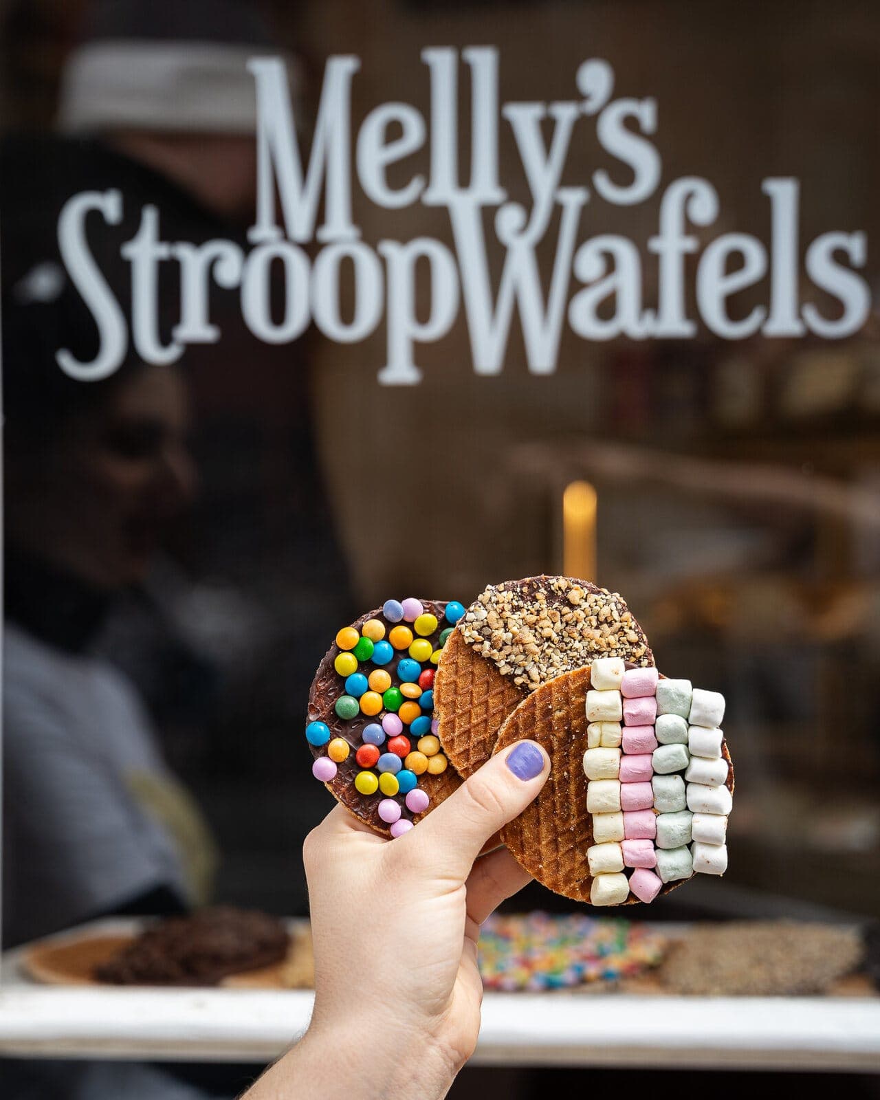 A hand holding freshly topped stroopwafels outside Melly's Stroopwafels in Amsterdam