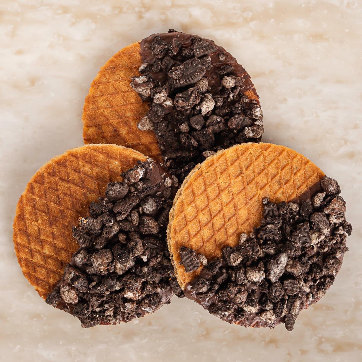 Three Melly's vegan stroopwafels dipped in dark chocolate and Oreo crumble