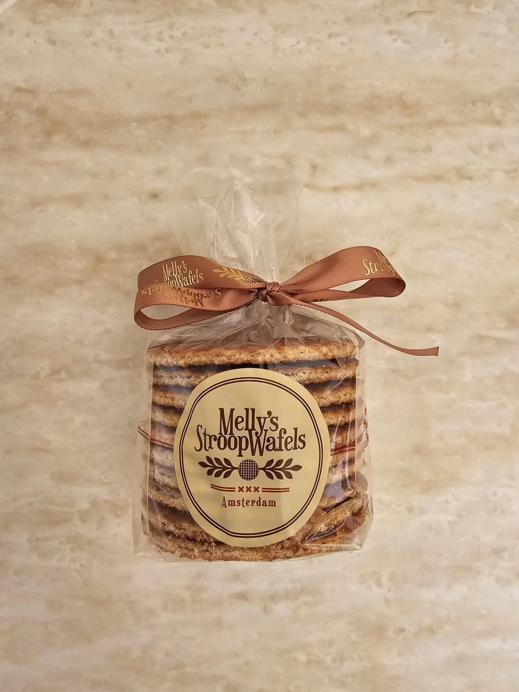 A stack of Melly's stroopwafels in a clear bag tied with a brown ribbon, on a marble counter