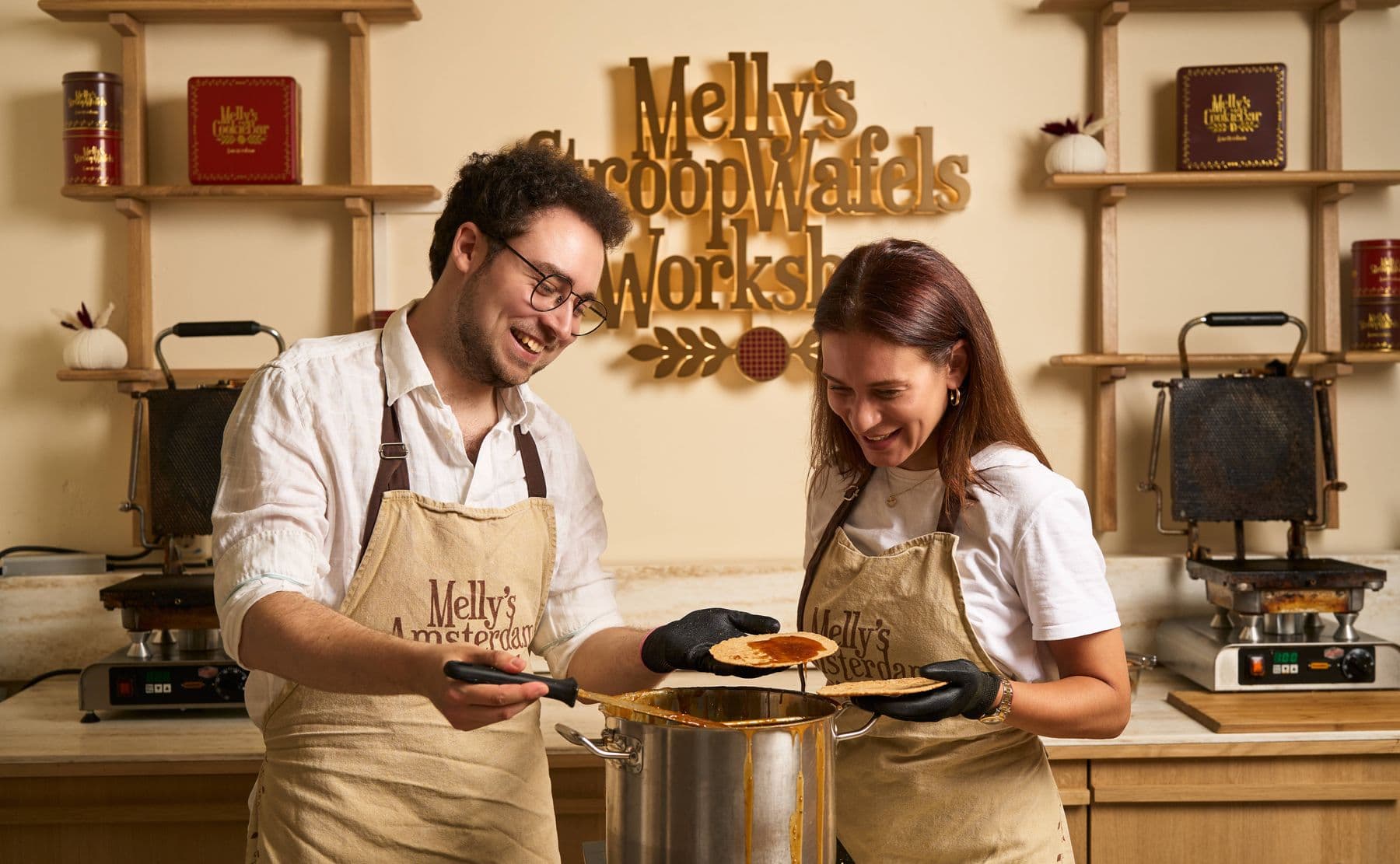 Zwei Gäste bei Mellys Stroopwafel-Workshop in Amsterdam gießen warmes Karamell auf eine frische Waffel