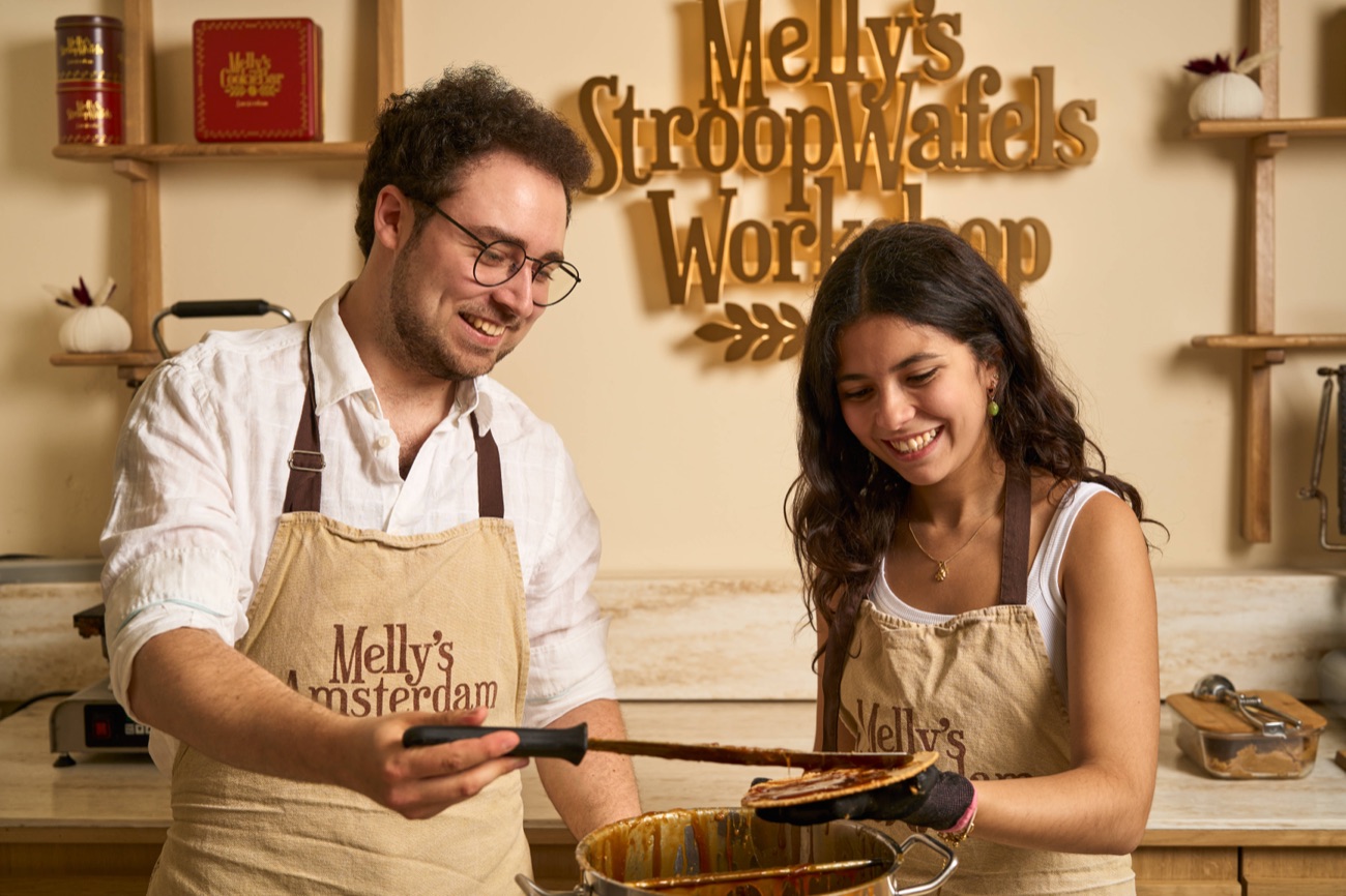 Two guests pressing a fresh stroopwafel on the iron at Melly's workshop in Amsterdam